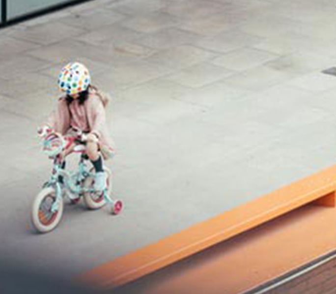 A little girl in a helmet rides her bicycle across an open paved court