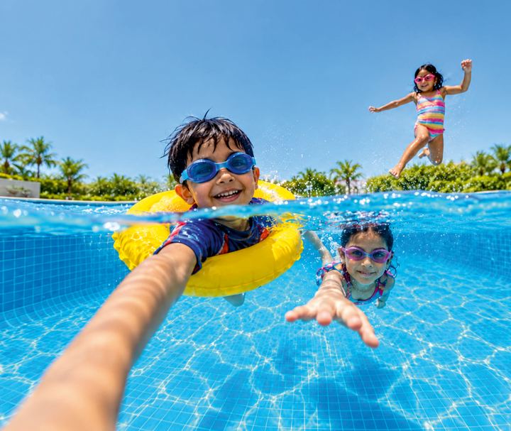 A boy in goggles and a float ring takes an underwater selfie in the swimming pool with his friends