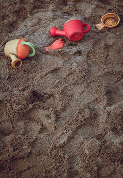 A toy watering can and buckets resting in a sand pit