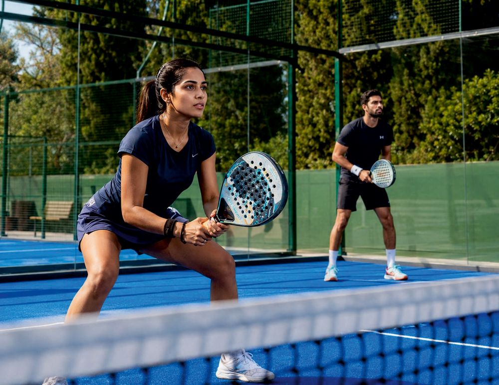 Two players on a blue padel-style court, one holding a racket ready to hit