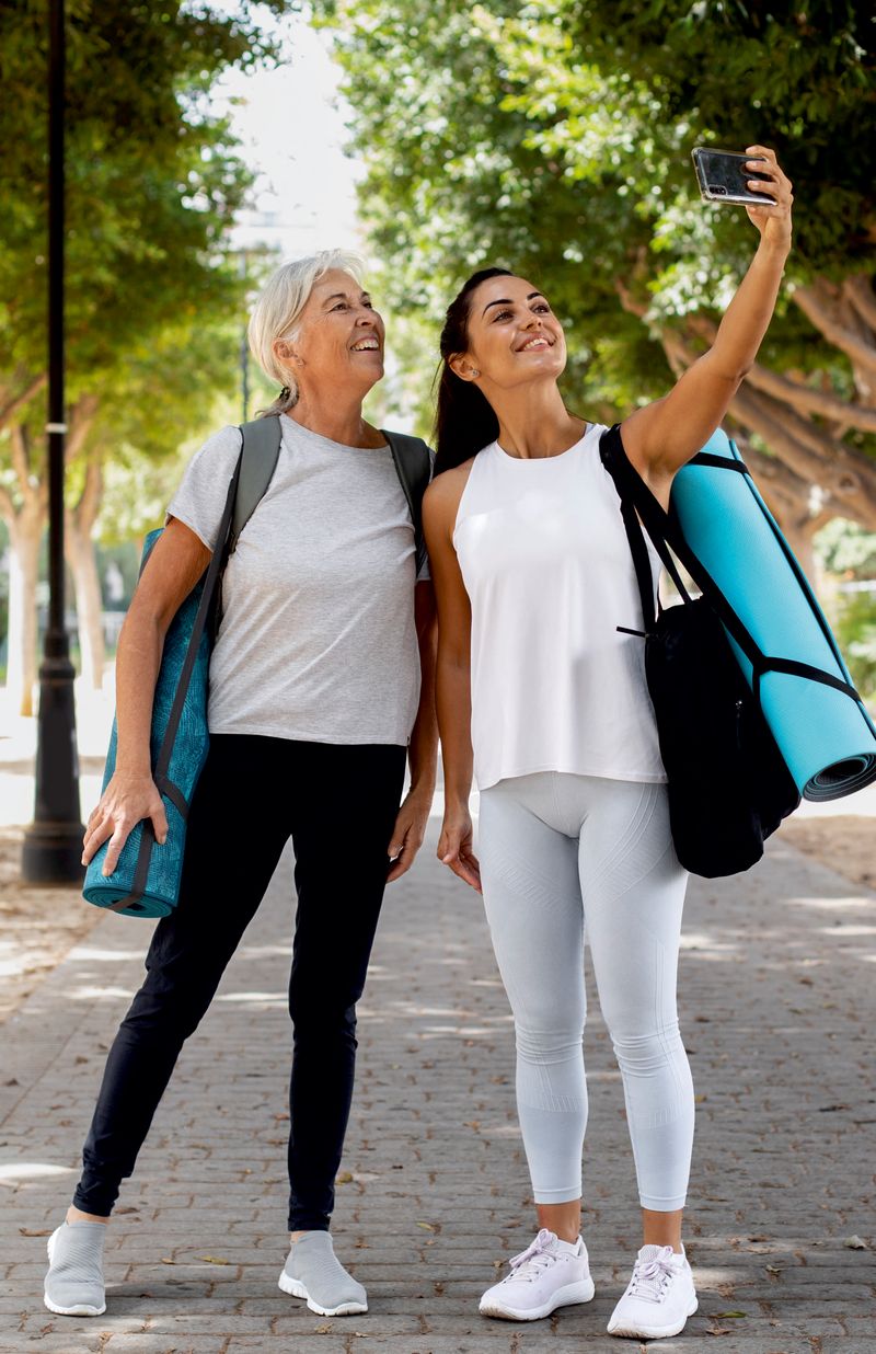 Two women taking a selfie on a walking path, one carrying a yoga mat