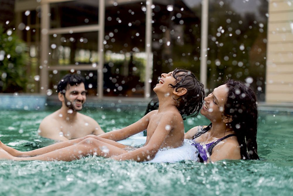 A family laughing and splashing together in a swimming pool